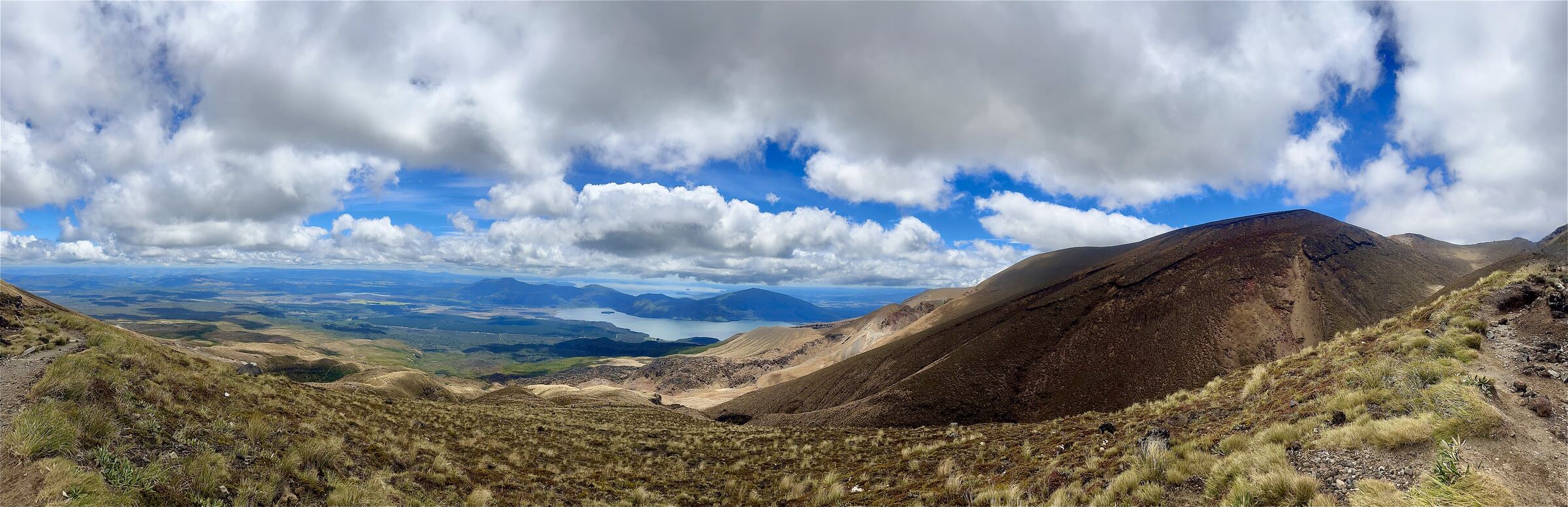 Panoramic view of a mountain valley and a distant lake under a bright, cloudy sky