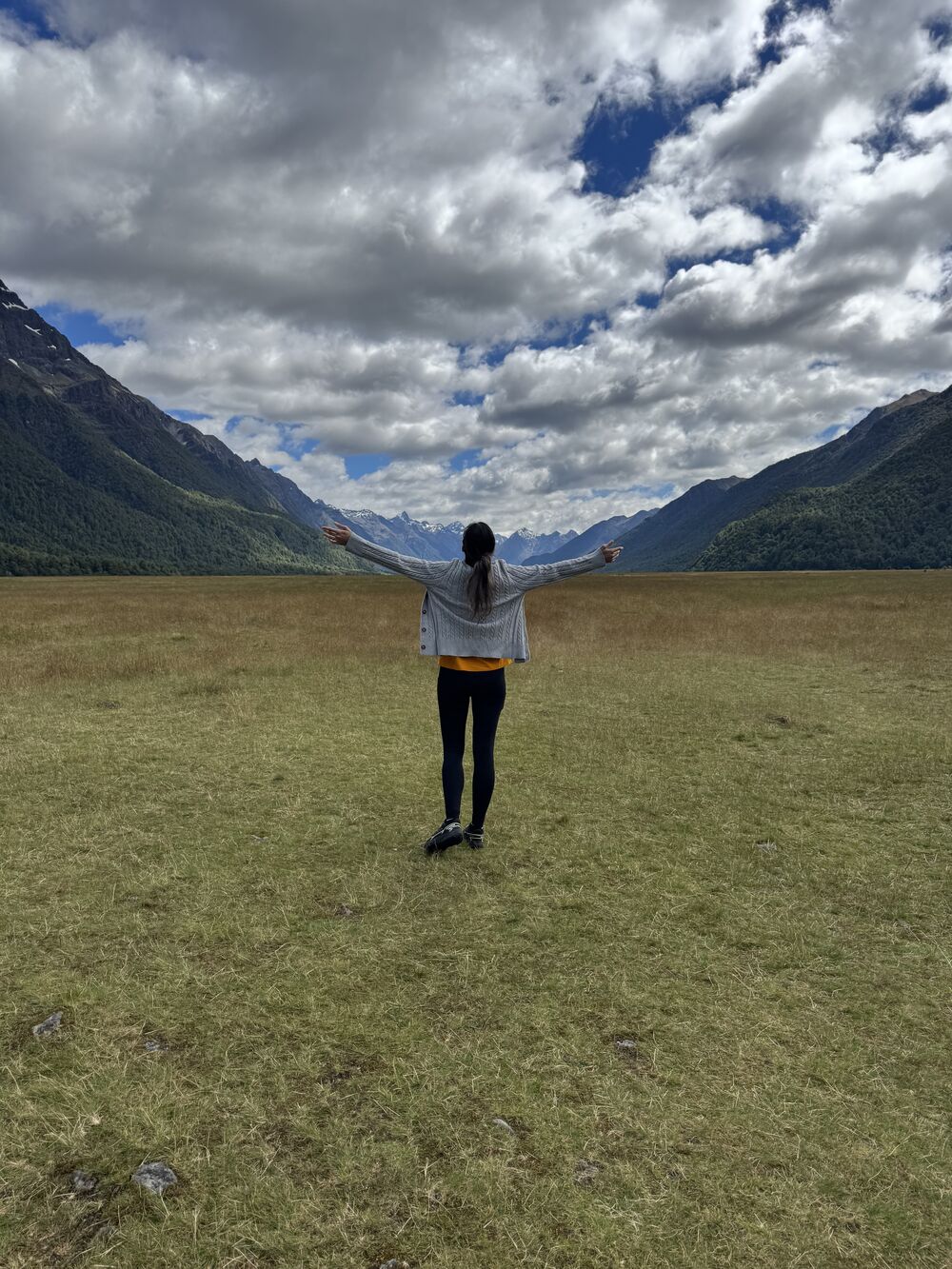 Mahnaz with arms outstretched on a grassy plain, surrounded by mountains