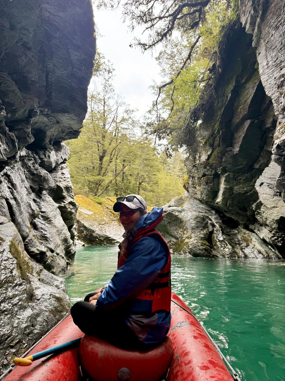 Mahnaz in a red inflatable raft between rocky walls above turquoise water